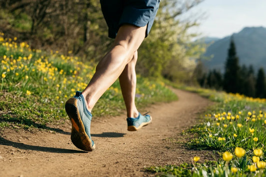 Runner in minimalist shoes on a natural trail surrounded by grass and flowers.